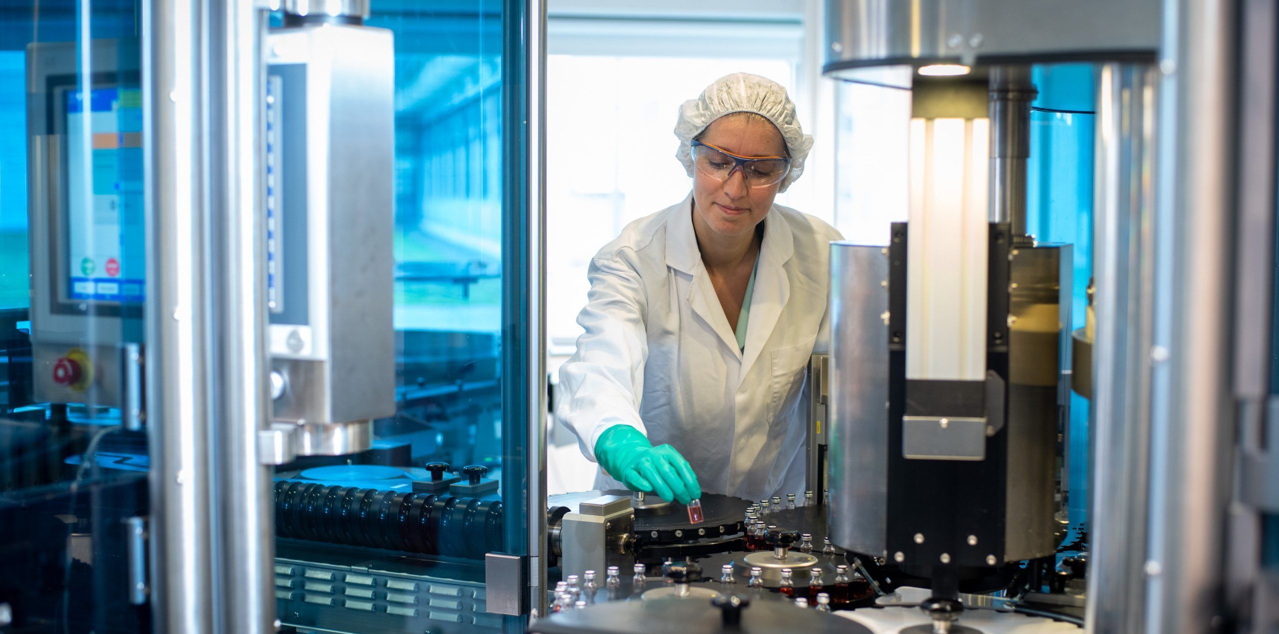 Vrouw in labjas en haarnetje zet een flesje in een machine