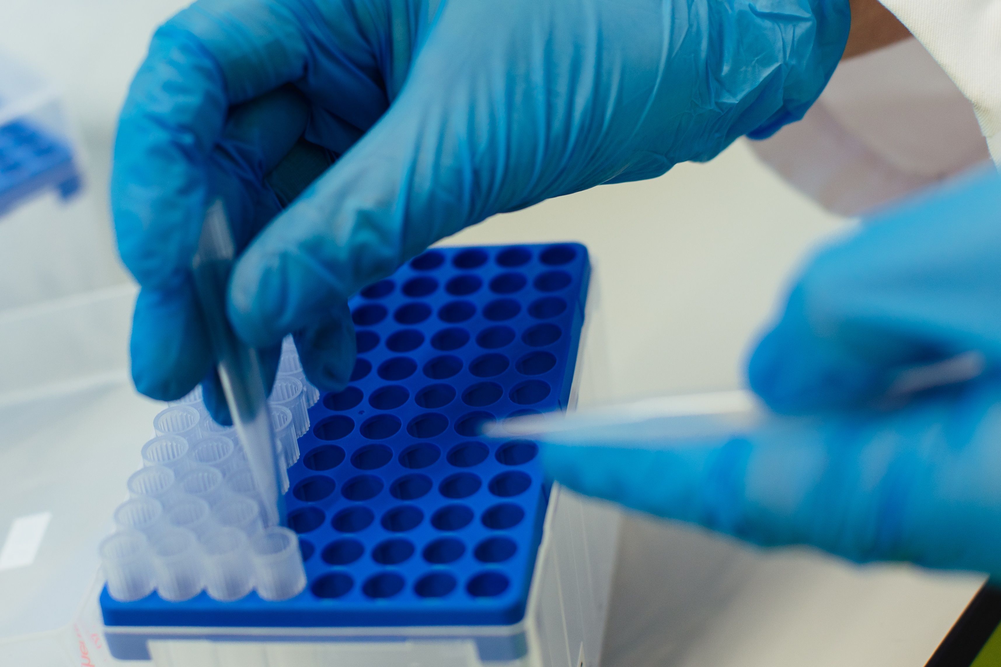 Een gehandschoende hand die een druppel in een reageerbuisje laat vallen